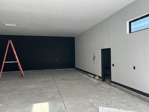 A concrete room with a black accent wall, gray walls, a ladder, and a window.