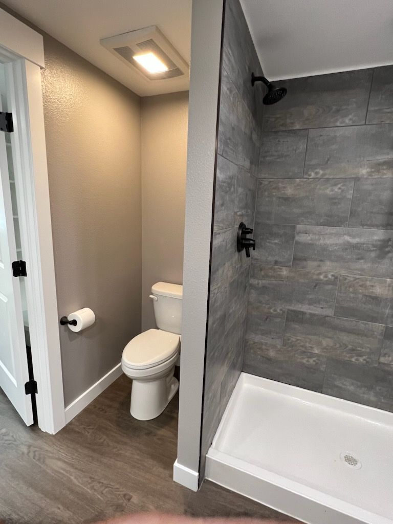 Bathroom with a toilet and a tiled shower. Gray and white color scheme.