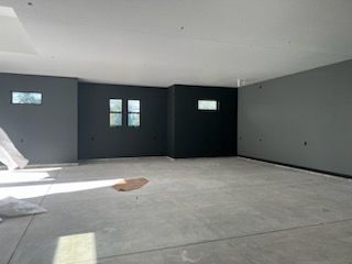 Empty room with concrete floor, dark gray and black walls, small windows, bright sunlight.