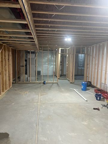 Basement under construction; wood framing, concrete floor, drywall, and building materials.