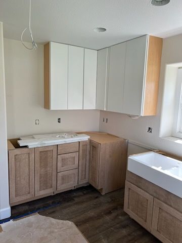 Kitchen cabinets: light wood lowers, white uppers, unfinished in construction, in a room with a window.