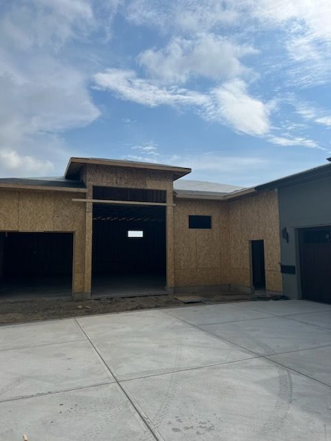 Construction of a modern home with an open garage under a cloudy sky. Wooden structure with concrete driveway.