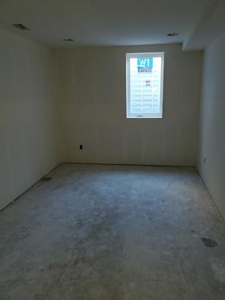 Empty unfinished room with a window; concrete floor and drywall walls.