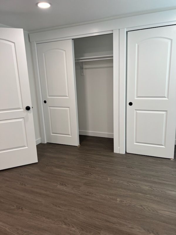 Bedroom with white doors and gray-brown flooring. Closet with a clothing rod is open.