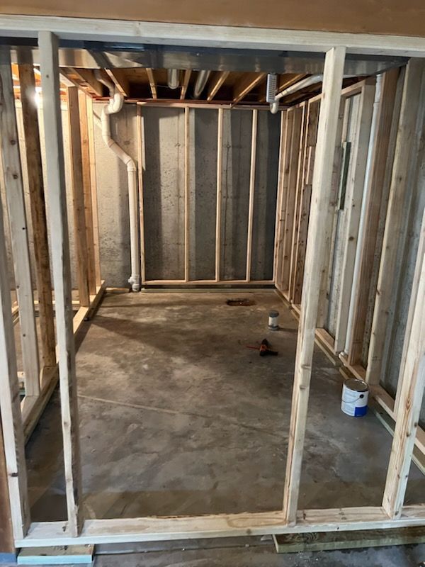 Unfinished room with wood framing on concrete floor. Plumbing pipes visible on the walls.