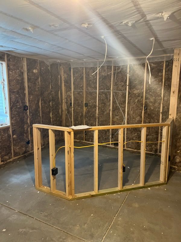 Basement room in progress, exposed studs, insulation, and partial wooden frame for a bar.