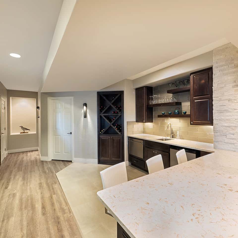 Basement bar with a countertop, dark cabinets, and a wine rack. Light wood floor and neutral walls.