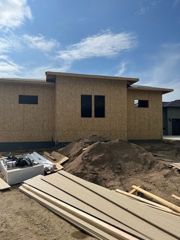Construction site. Unfinished house with plywood siding, windows, and materials in front. Overcast sky.