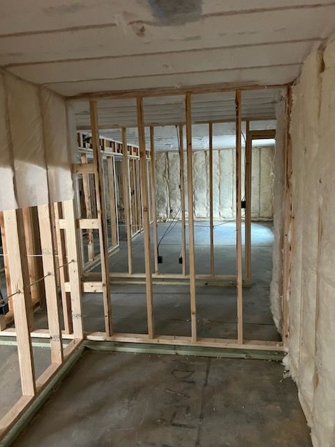Framed wooden walls in a concrete basement under construction, with insulation visible on the right.