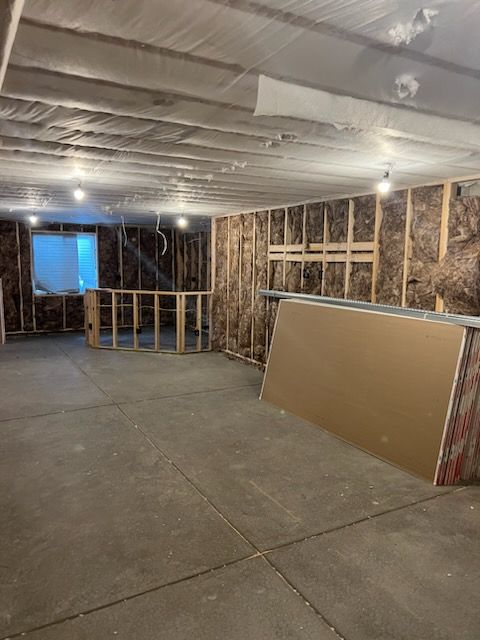 Basement under construction with exposed framing, insulation, and drywall. Concrete floor and unfinished ceiling.