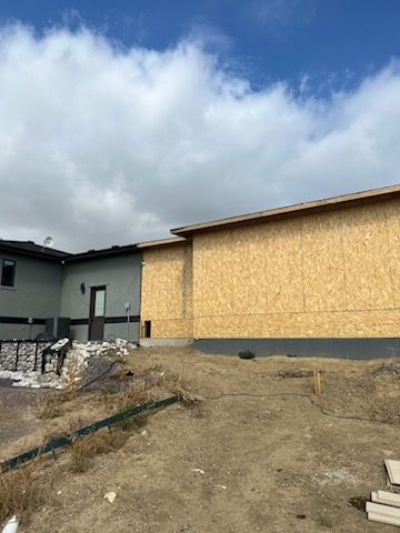 Building under construction with wooden siding, gray exterior and a cloudy sky.