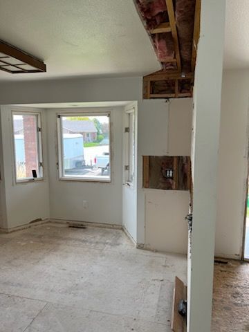 Room undergoing renovation with exposed drywall, wiring, and a bay window.