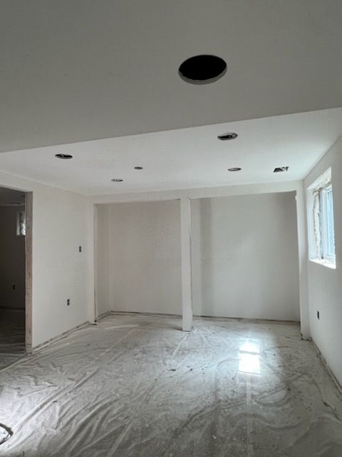 Interior room with white walls, ceiling, and concrete floor covered in plastic sheeting. 