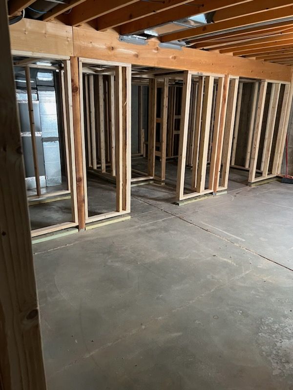 Basement renovation in progress; wooden studs frame walls, concrete floor.