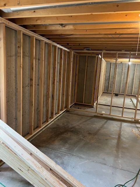 Basement under construction with exposed wooden framing, concrete floor, and unfinished walls.