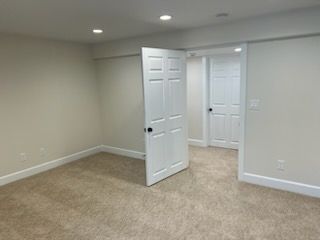 Empty beige carpeted room with open white doors, leading to another room.