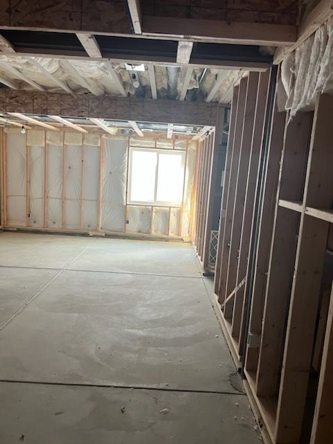 Unfinished room with concrete floor, window, wooden studs, and exposed ceiling beams; construction in progress.