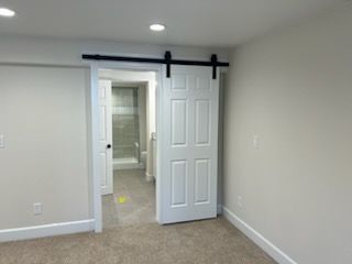 White barn door on a black track, open to a hallway and bathroom. Beige walls and carpet.