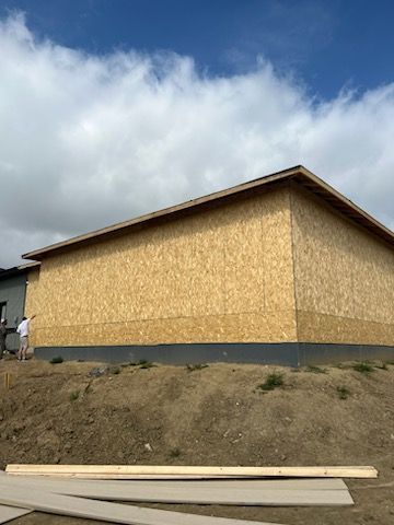 Building under construction with OSB siding against a blue sky with clouds. A person stands near the side.