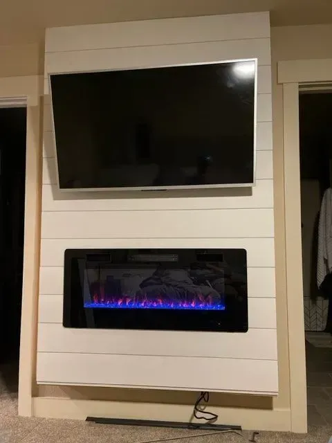 White shiplap wall with mounted TV and electric fireplace, with cables and a door in the background.