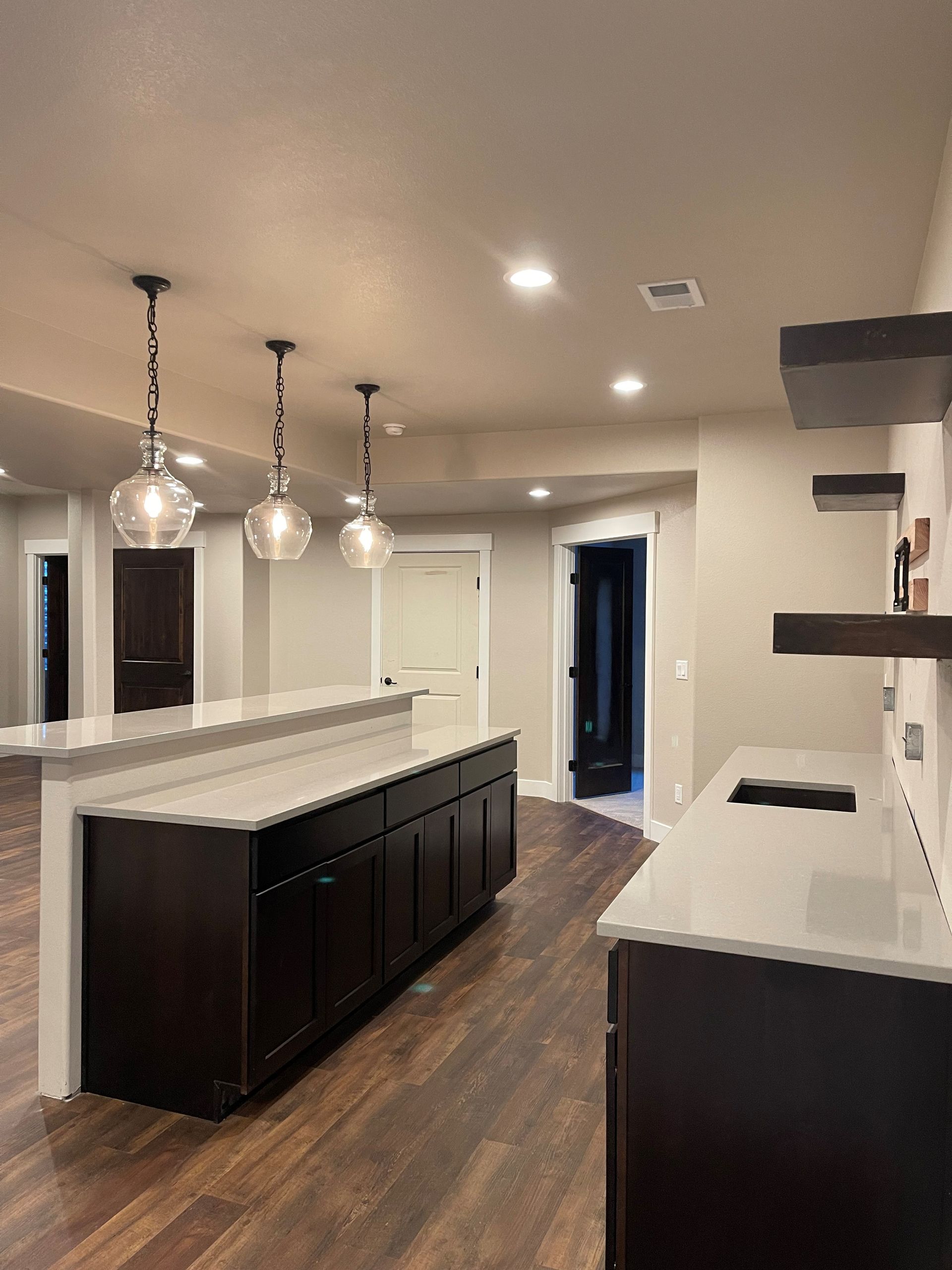 Modern kitchen/bar area with dark cabinetry, light countertops, wood floors, and pendant lights.
