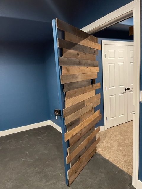 Wooden-paneled door partially open in a room with blue walls and a white door across the hall.