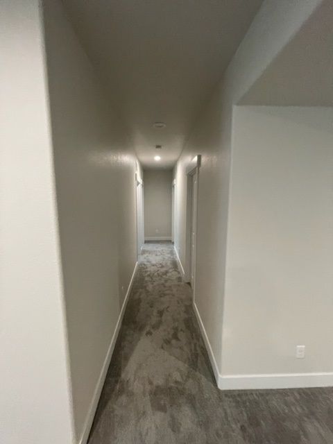 Narrow, beige hallway with gray carpet, white walls, and doors.