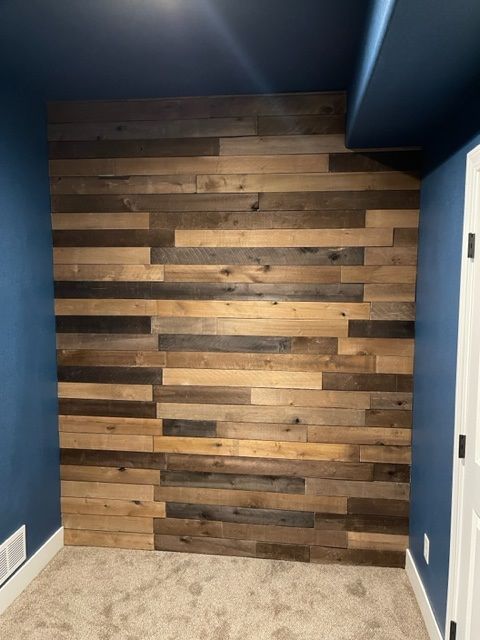 Wooden plank accent wall with various brown and tan shades, blue painted walls, and carpeted floor.
