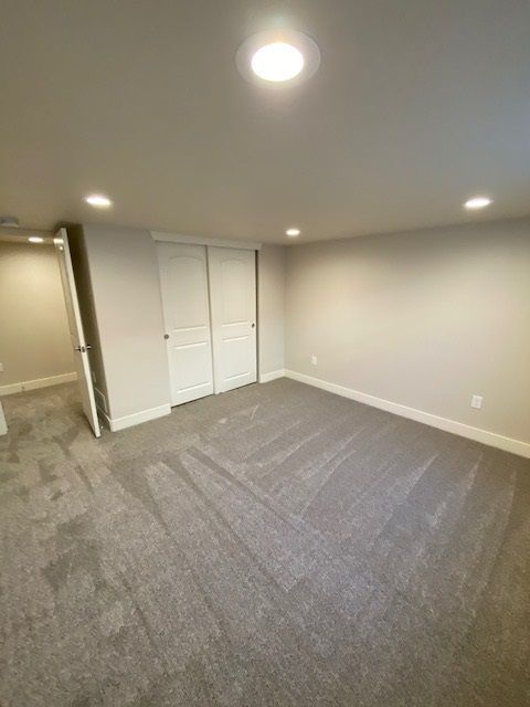 Empty bedroom with grey carpet, white closet doors, and recessed lighting.