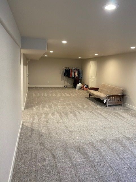 Empty carpeted basement with a futon, clothing rack, and recessed lighting.
