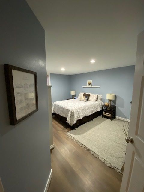 Bedroom with blue walls, bed with white comforter, rug, and art on wall.