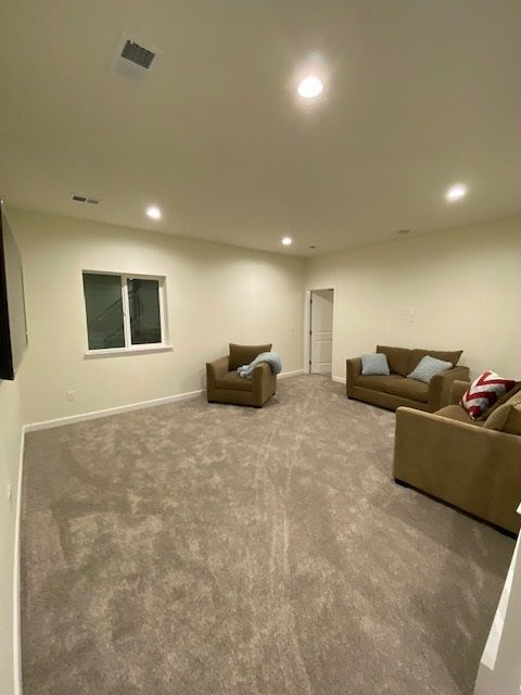 Empty living room with tan carpet, brown furniture, and white walls.