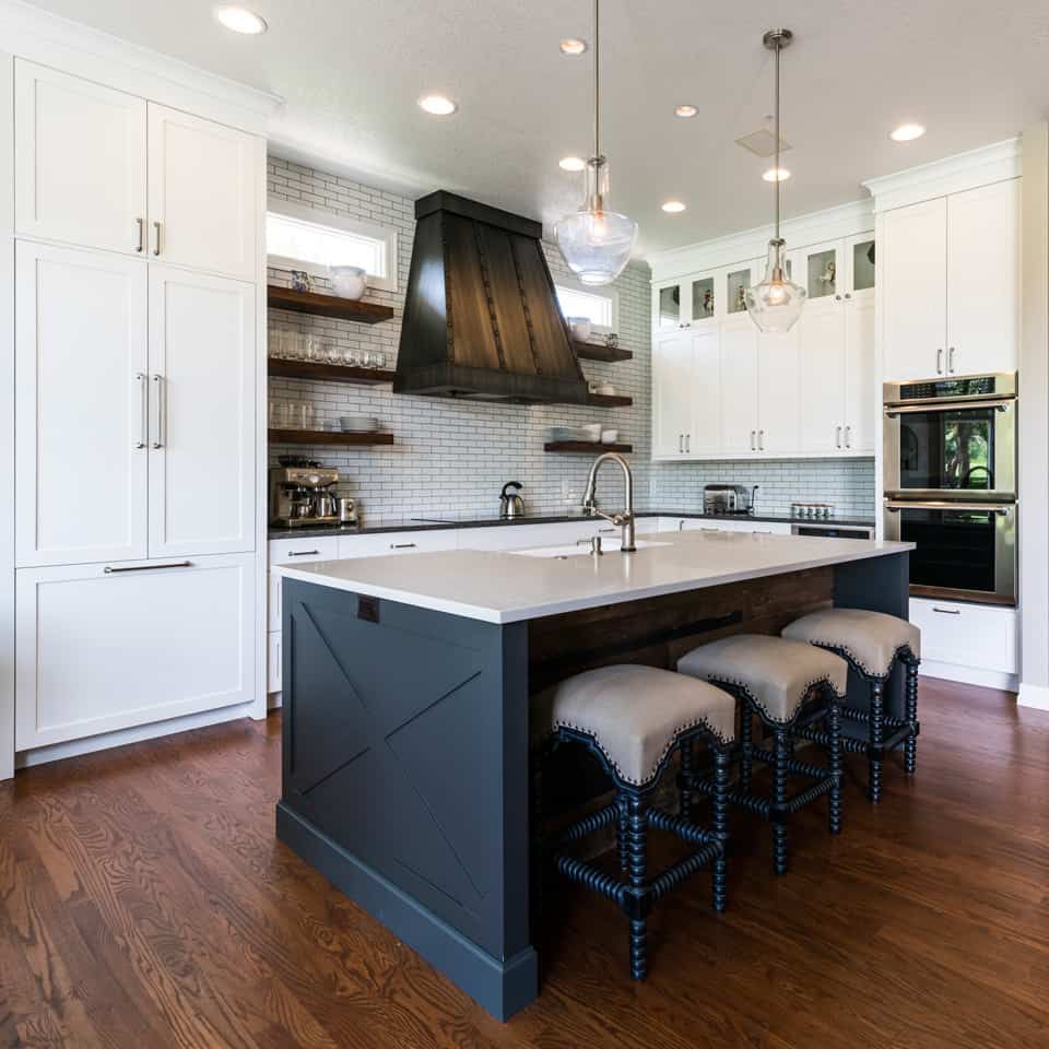 Modern kitchen with white cabinets, dark island with stools, and wooden floors.