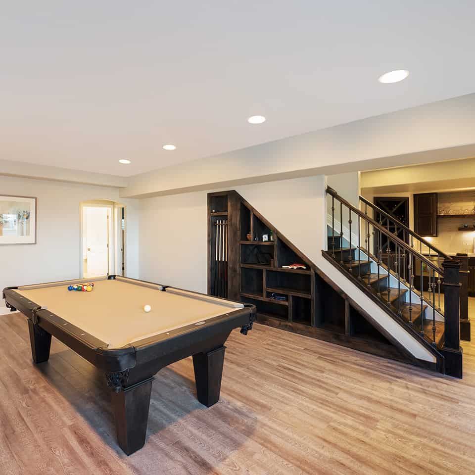 A finished basement with a pool table, staircase, and built-in shelving.