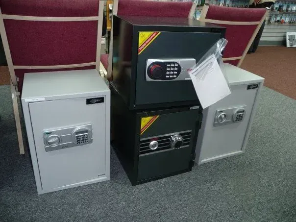 Four metal safes with electronic keypads are displayed on a carpeted floor.