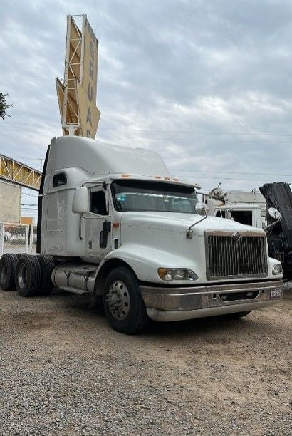 Un camión semirremolque blanco está estacionado en un lote de grava frente a un edificio.