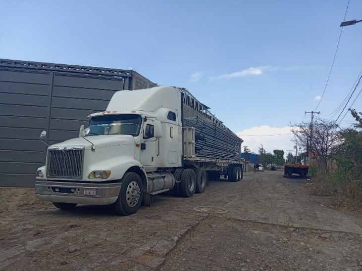 Un camión semirremolque blanco está estacionado en un lote de tierra frente a un edificio.