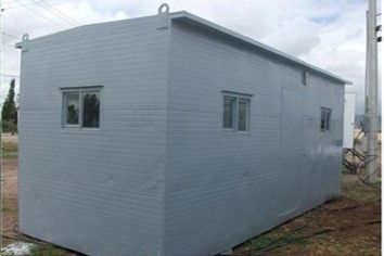 Un edificio gris con dos ventanas está situado en medio de un campo.