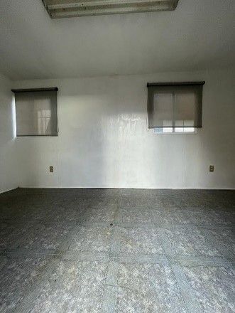 Una habitación vacía con dos ventanas y un suelo gris.