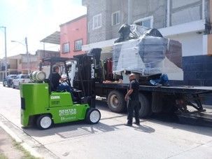 Una carretilla elevadora verde está cargando una máquina grande en un camión de plataforma.