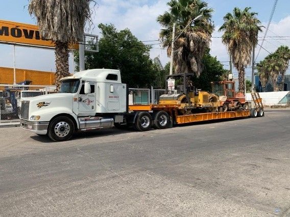 Un camión semirremolque blanco lleva un remolque con un tractor amarillo encima.