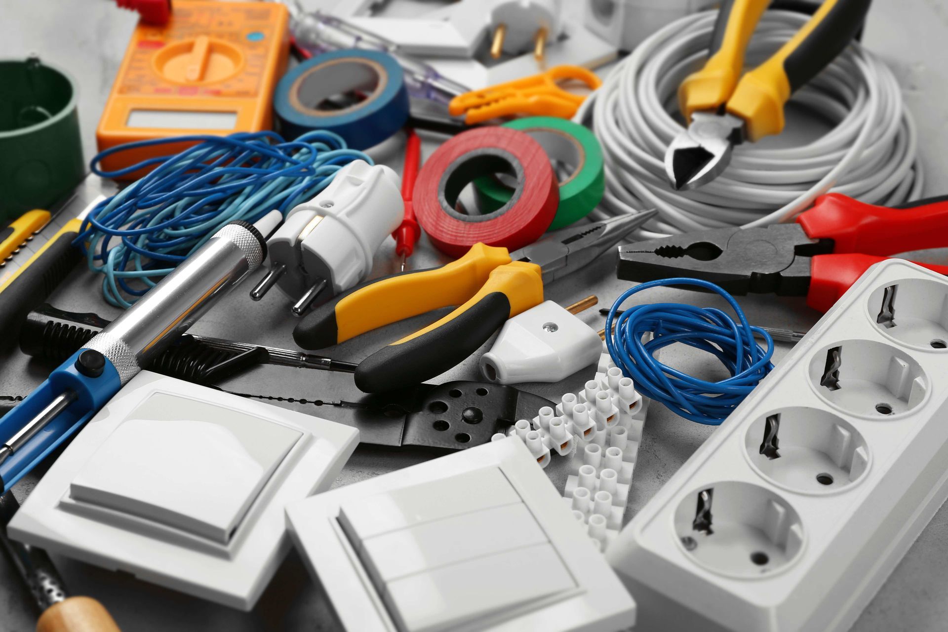 Assorted electrical tools and supplies, including wires, plugs, outlets, tape, and switches, on a white surface