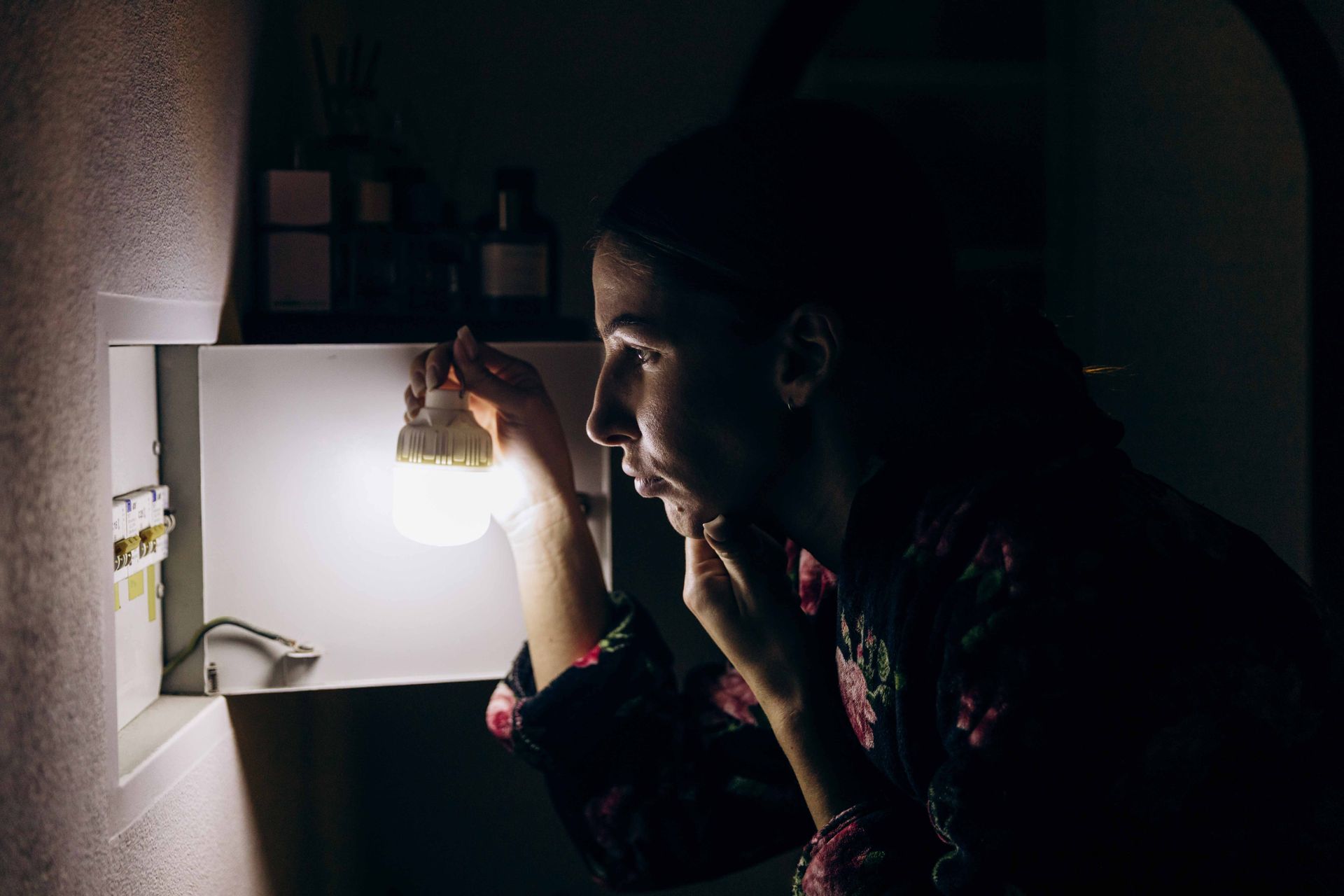 Person adjusting a hanging light bulb in a dim room, lit by the glow of the lamp.
