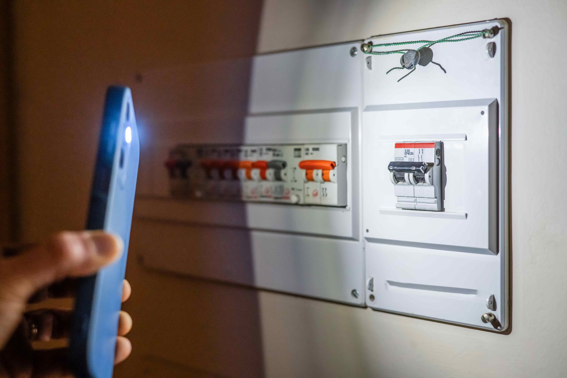 Hand holding a smartphone near an open electrical breaker panel with switches and wiring