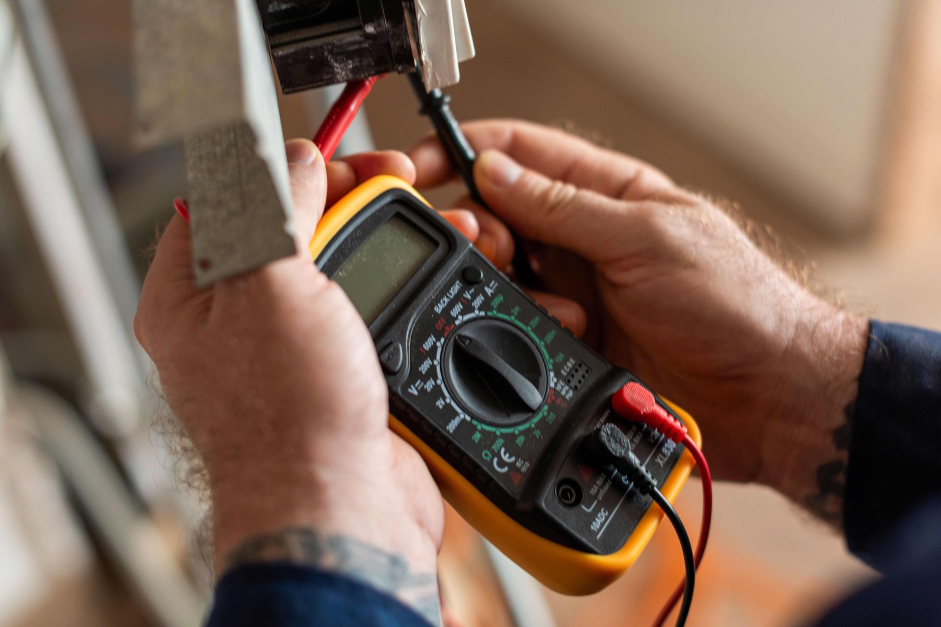 Hands using a digital multimeter to test wiring on an electrical panel