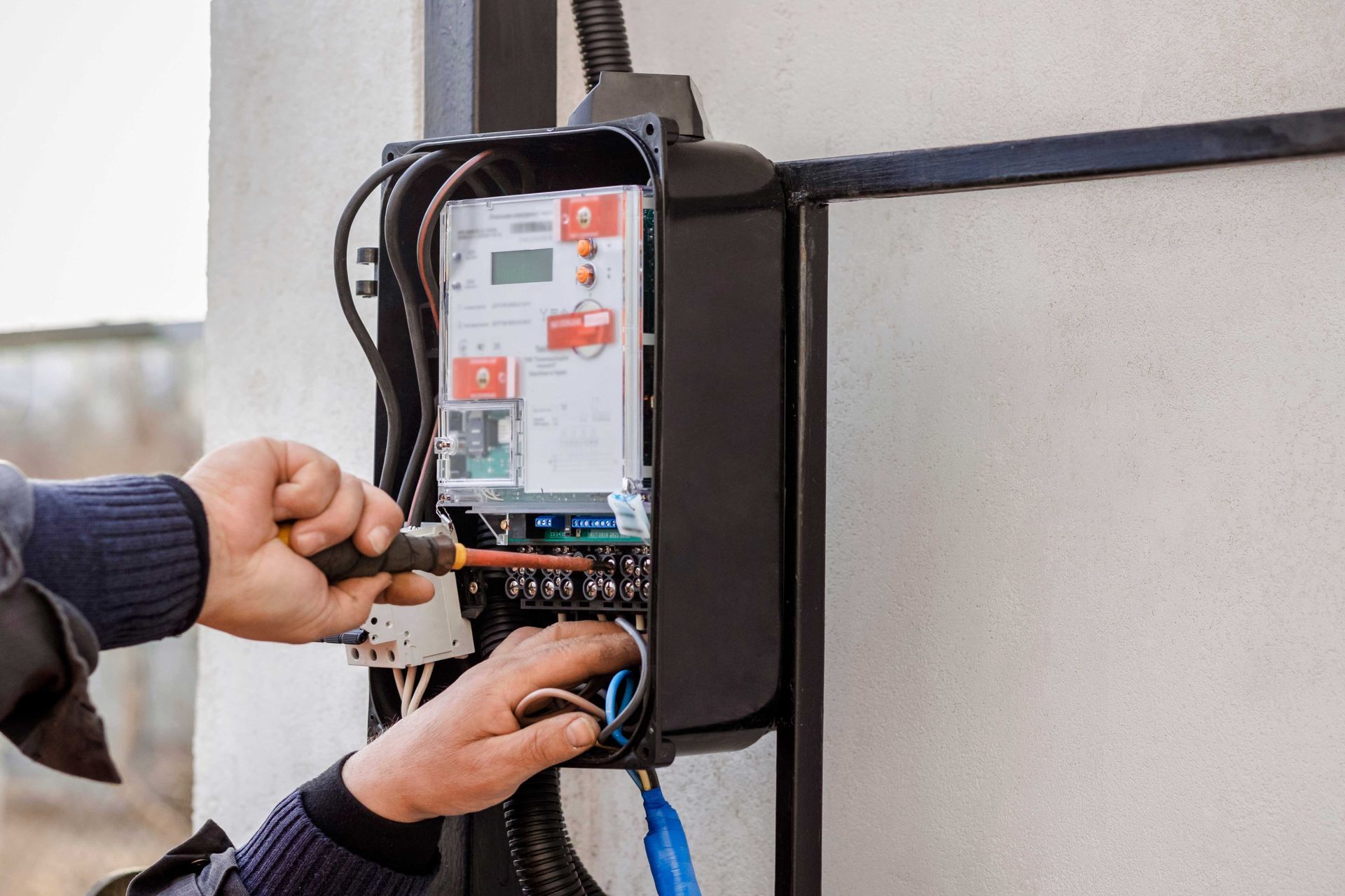 Hands wiring a wall-mounted electrical panel with tools and blue cable