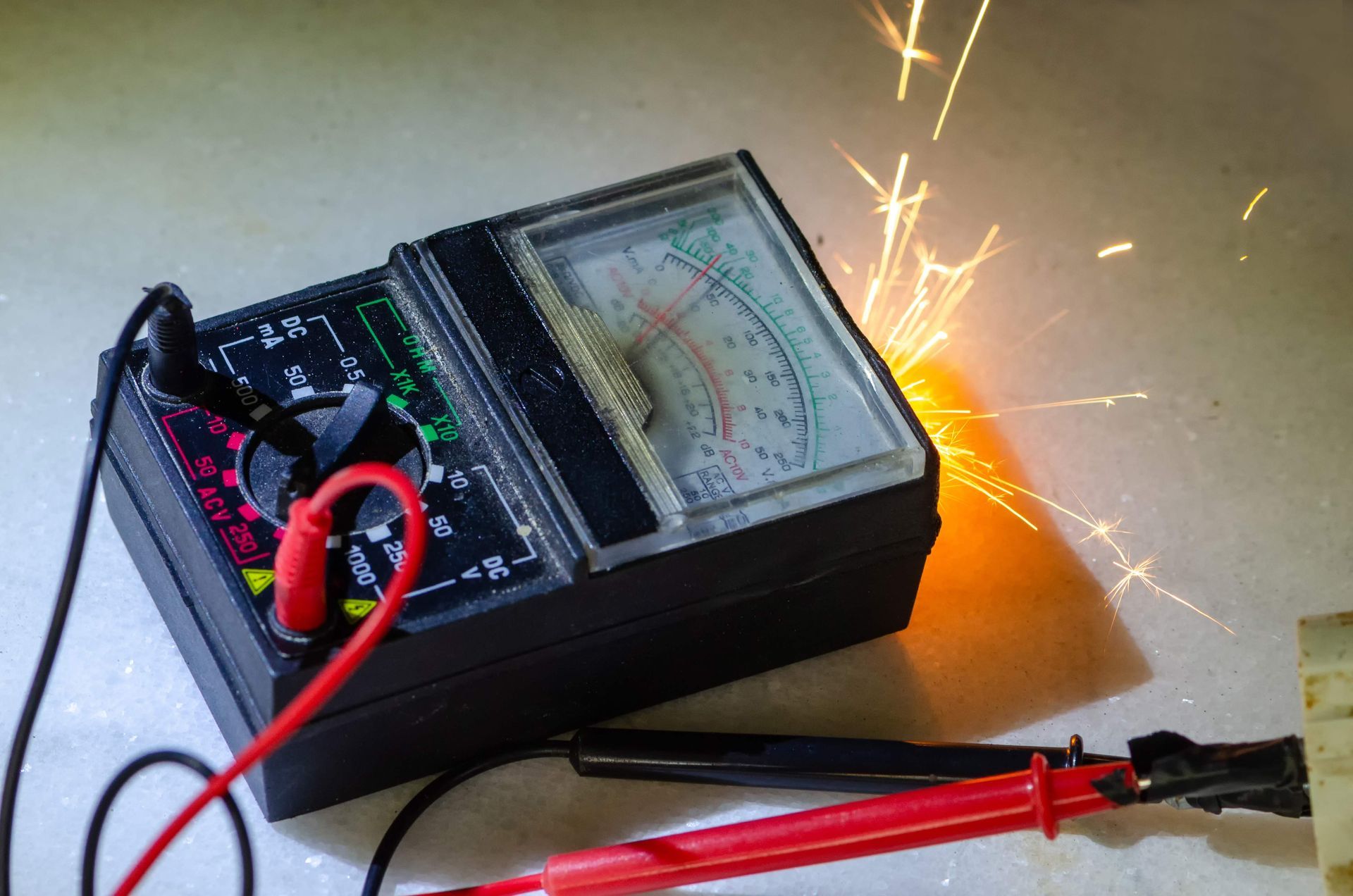 Analog multimeter with red probes sparking on a wire, creating bright sparks on a tabletop