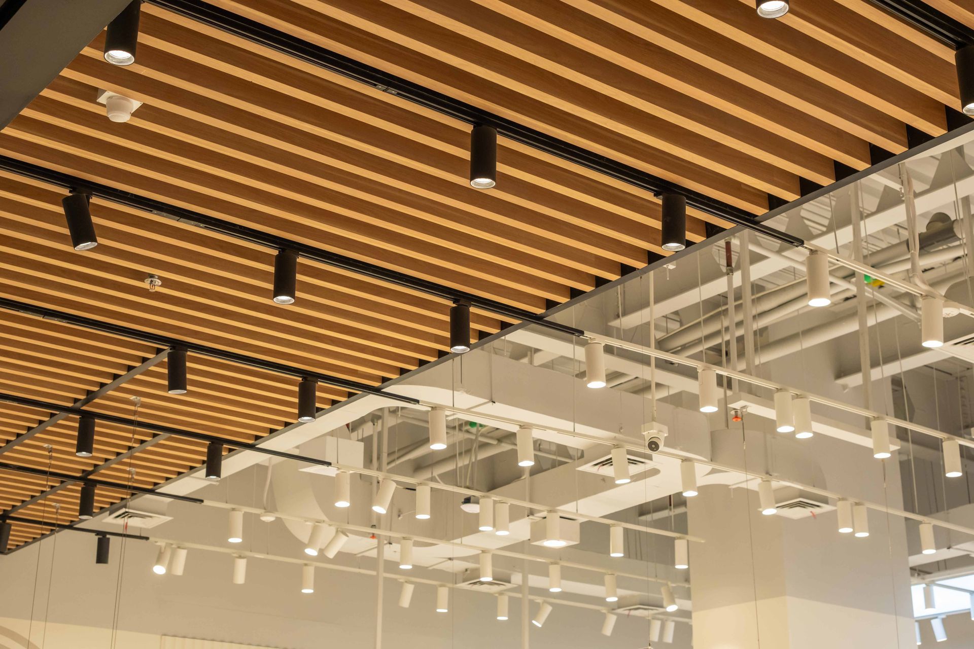 Modern interior ceiling with wooden slats, white beams, and hanging black lights