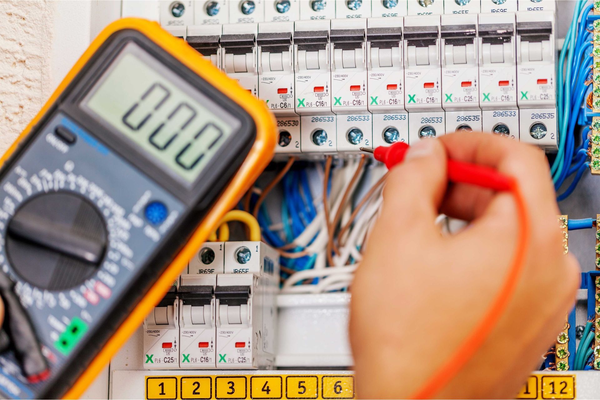 Digital multimeter testing wiring in an electrical circuit breaker panel with numbered switches.
