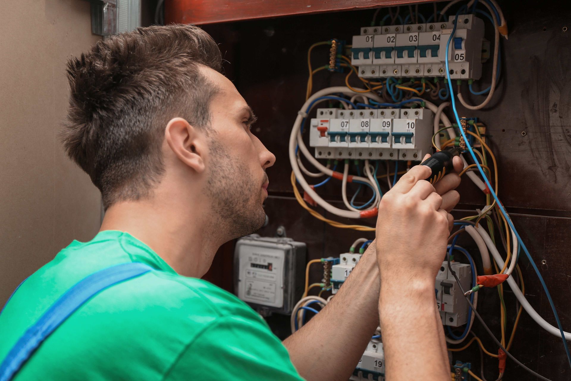 Technician in a green shirt inspecting electrical wiring inside an open panel